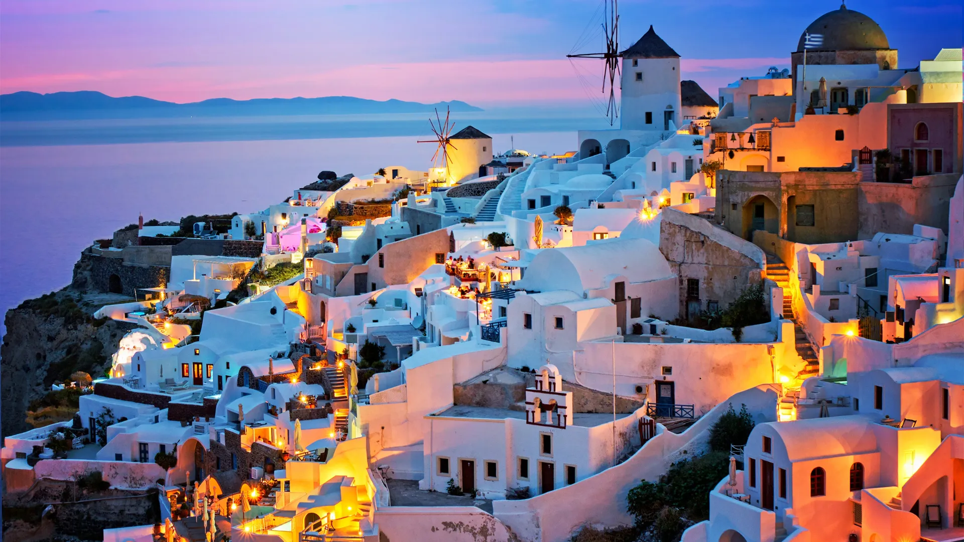 Beleuchtete Windmühlen und weiße Häuser in Oia auf Santorini bei Einbruch der Nacht