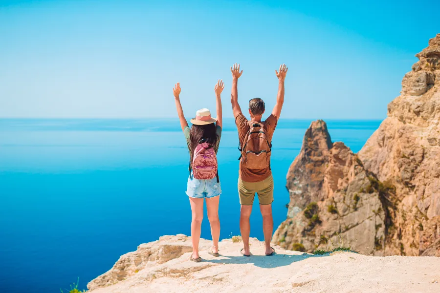 Zwei Reisende mit erhobenen Armen an einem Aussichtspunkt über dem Meer – Star Reisen